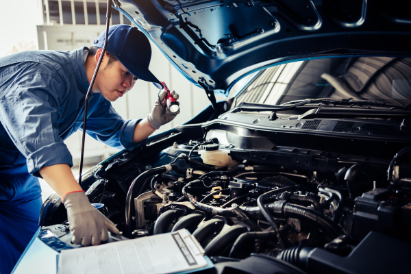 Mechanic using a flashlight to inspect a car engine in a workshop.