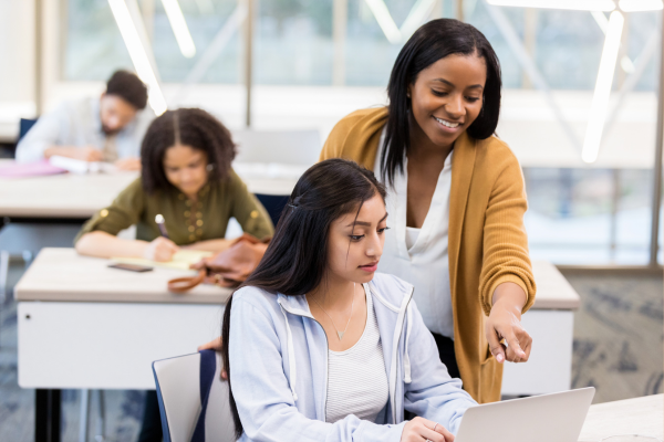 Diverse teacher assisting a student, highlighting educator recruitment.