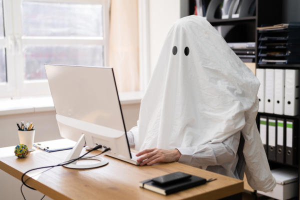 A person dressed as a ghost sitting at a desk with a computer.