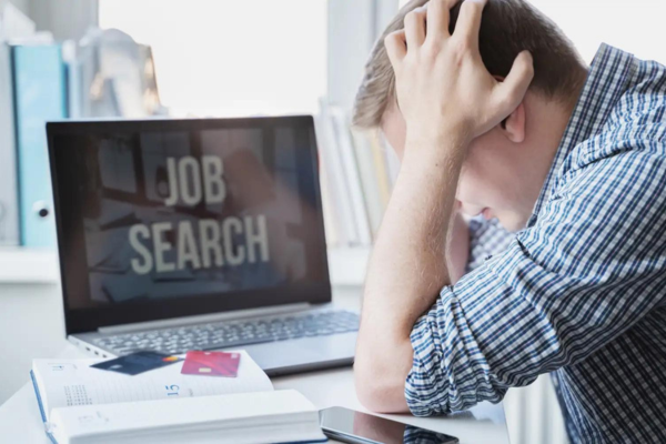 Man holding his head in frustration while searching for jobs online.