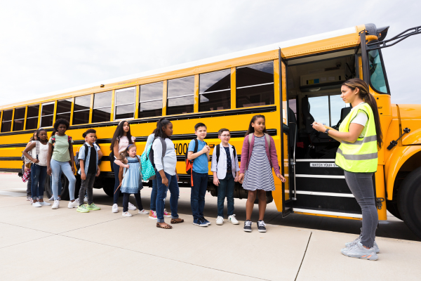 School bus driver with students lined up to board the bus, illustrating bus driver recruiting.