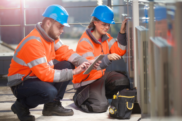 Two HVAC professionals in safety gear training on commercial HVAC units, showcasing the importance of certifications.