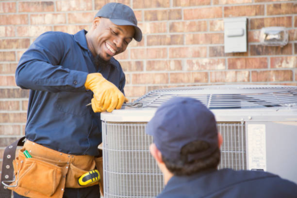 Two HVAC technicians working on an outdoor unit, representing strong company culture and teamwork in the HVAC industry.