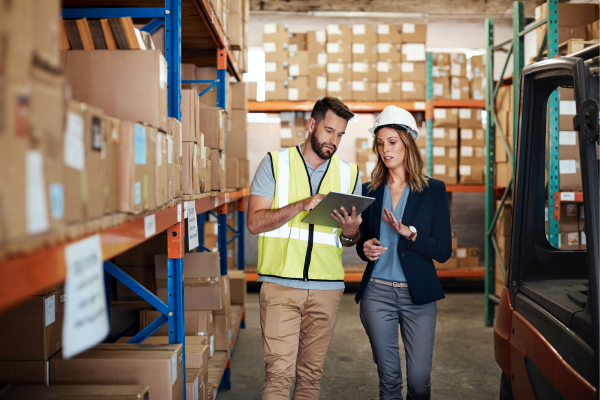 Logistics manager and worker reviewing inventory in a warehouse.