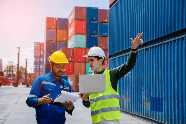 Two logistics workers discussing operations in front of shipping containers.