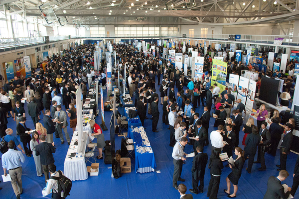 A bustling career fair with recruiters and candidates networking, showcasing how industry events can aid in finding a job recruiter.